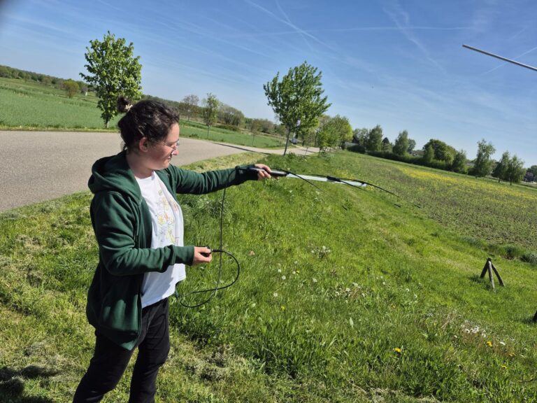 Ecoloog richt een handantenne op een veld tijdens telemetrie-onderzoek naar vleermuizen